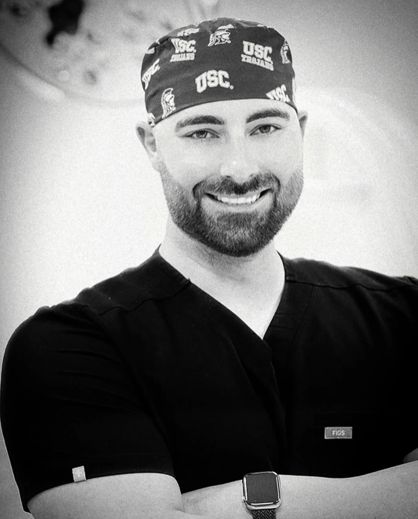 Dr. Efe Ozturk smiling, in black scrubs and a USC surgical cap